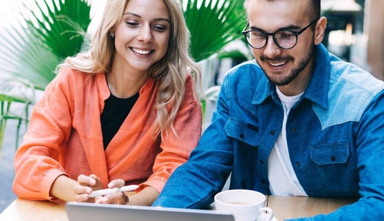 Two adults smiling at a laptop on an outdoor work table.