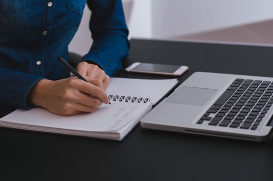 Person sitting at a table and taking notes on a notebook.