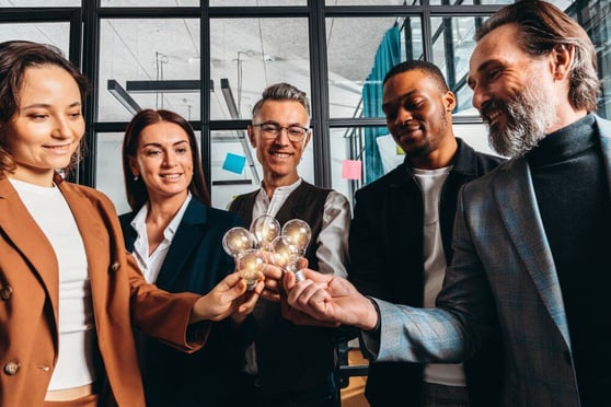 People smiling, in a circle, holding lit lightbulbs.