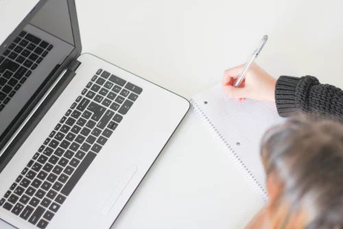 Persona sentada en un escritorio, con un bloc de notas y una computadora portátil abierta.