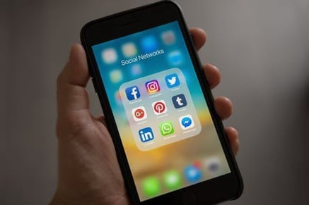 Mano sosteniendo un teléfono celular, con iconos de redes sociales en la pantalla