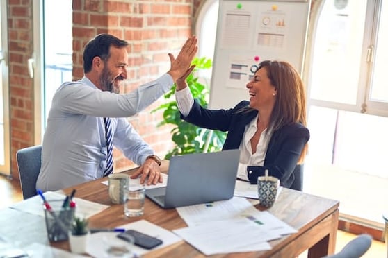 Two people at a desk, high fiving and smiling.