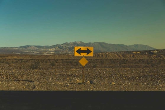 Yellow road sign in a desert road, pointing left and right.