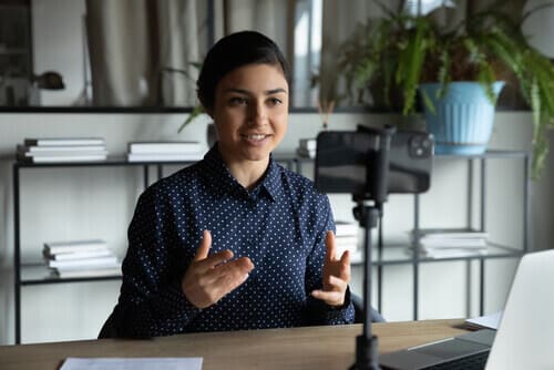 Person sitting at a table, talking to a camera standing on a tripod.
