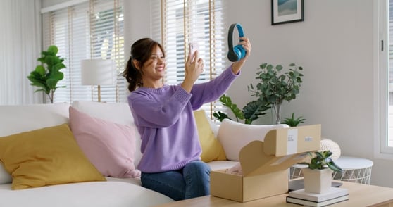 Woman on a couch, taking photo of pair of blue headphones.