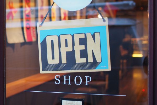 Photo of the door of a business with an OPEN sign hanging on it.